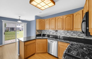 kitchen with sink, hanging light fixtures, light hardwood / wood-style flooring, kitchen peninsula, and black appliances