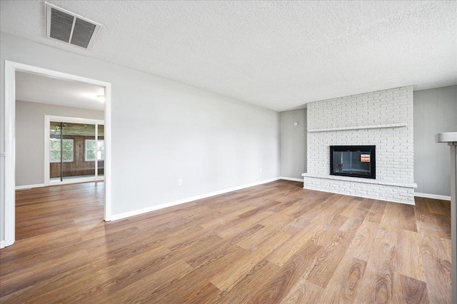 unfurnished living room with wood-type flooring, a textured ceiling, and a brick fireplace