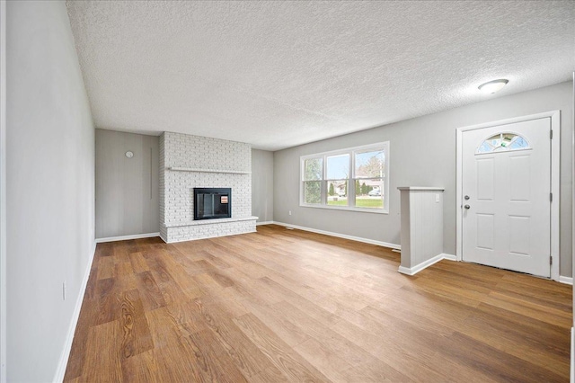 unfurnished living room with wood-type flooring, a textured ceiling, and a brick fireplace