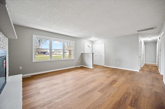 unfurnished living room with a brick fireplace, a textured ceiling, and light wood-type flooring