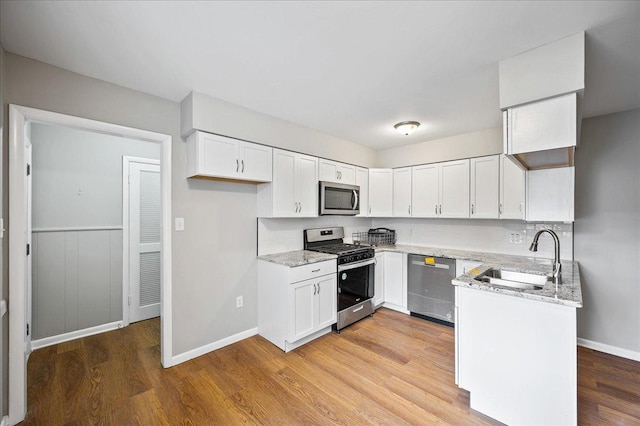 kitchen with light stone countertops, appliances with stainless steel finishes, light wood-type flooring, sink, and white cabinets