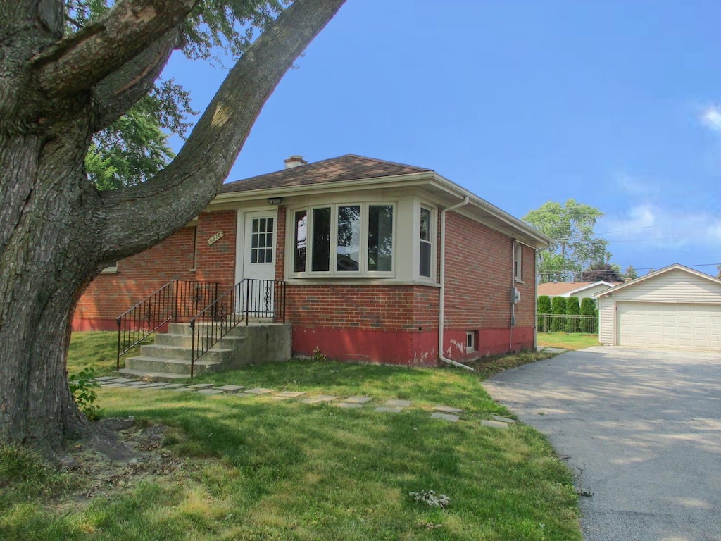 bungalow-style home featuring a garage, an outdoor structure, and a front lawn