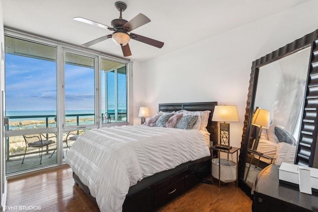 bedroom with expansive windows, a water view, hardwood / wood-style flooring, ceiling fan, and access to exterior