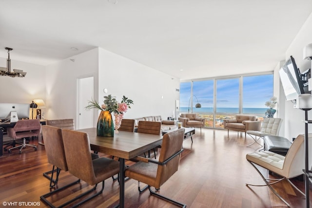 dining space featuring dark hardwood / wood-style flooring, a water view, a chandelier, and a wall of windows