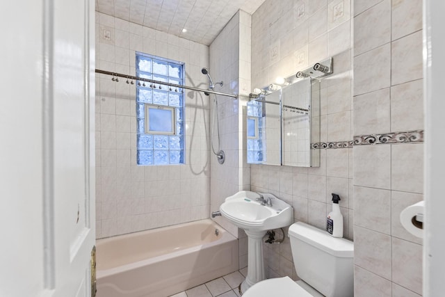 bathroom featuring toilet, tiled shower / bath combo, tile patterned floors, and tile walls