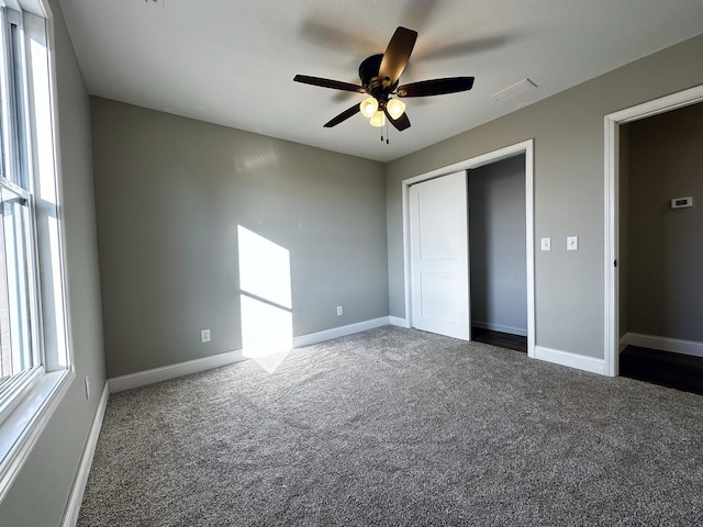 unfurnished bedroom with multiple windows, ceiling fan, a closet, and dark colored carpet