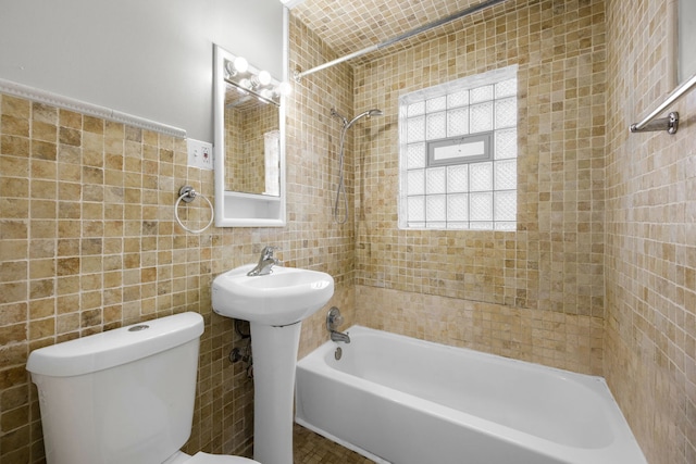 bathroom with tiled shower / bath combo, toilet, and tile walls