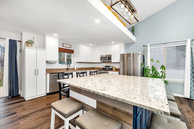 kitchen with appliances with stainless steel finishes, a kitchen island, dark hardwood / wood-style flooring, white cabinetry, and a breakfast bar area