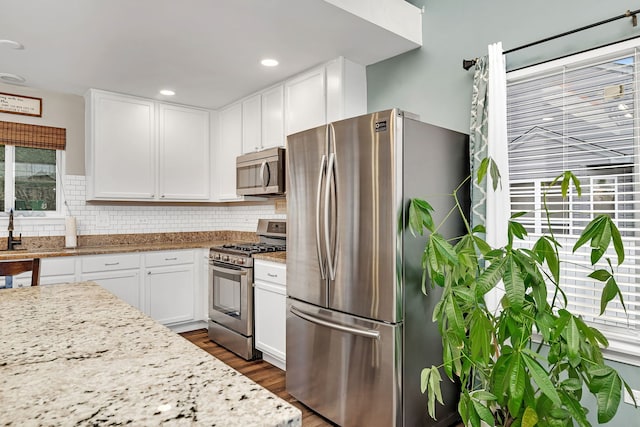 kitchen with white cabinetry, light stone countertops, dark wood-type flooring, tasteful backsplash, and appliances with stainless steel finishes