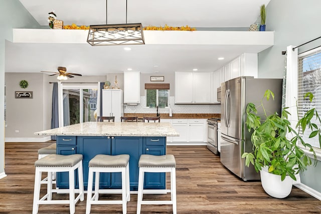 kitchen with a kitchen breakfast bar, stainless steel appliances, white cabinets, a kitchen island, and hanging light fixtures