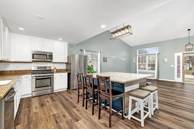 kitchen featuring white cabinetry, stainless steel appliances, vaulted ceiling, decorative light fixtures, and a kitchen island