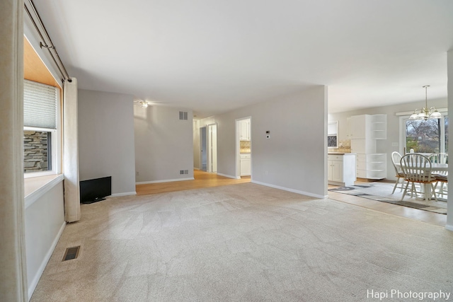 unfurnished living room featuring a chandelier and light colored carpet