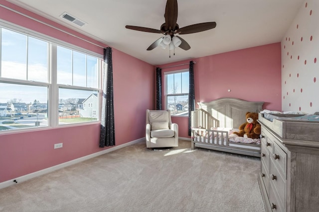 bedroom with ceiling fan, light colored carpet, a crib, and multiple windows