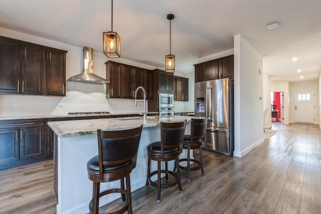 kitchen with a kitchen island with sink, hardwood / wood-style floors, wall chimney exhaust hood, and stainless steel appliances