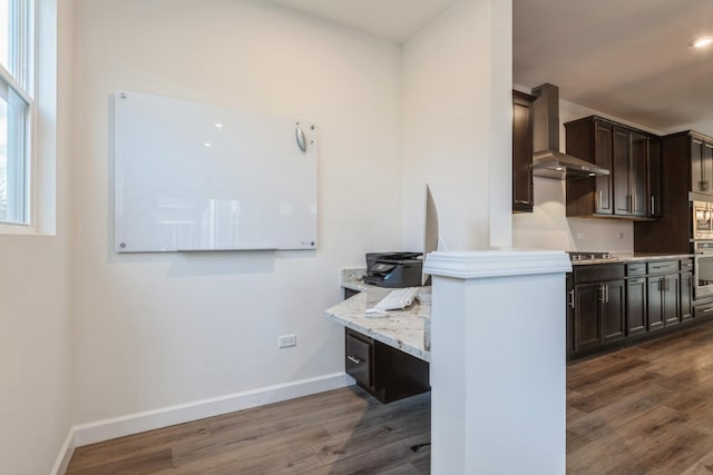 kitchen with dark brown cabinetry, wall chimney range hood, light stone counters, dark hardwood / wood-style flooring, and appliances with stainless steel finishes