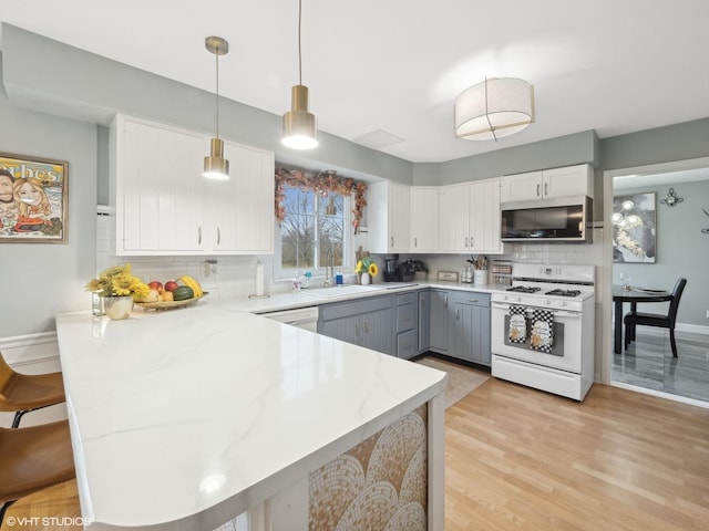 kitchen featuring kitchen peninsula, white gas range, gray cabinetry, decorative light fixtures, and white cabinetry