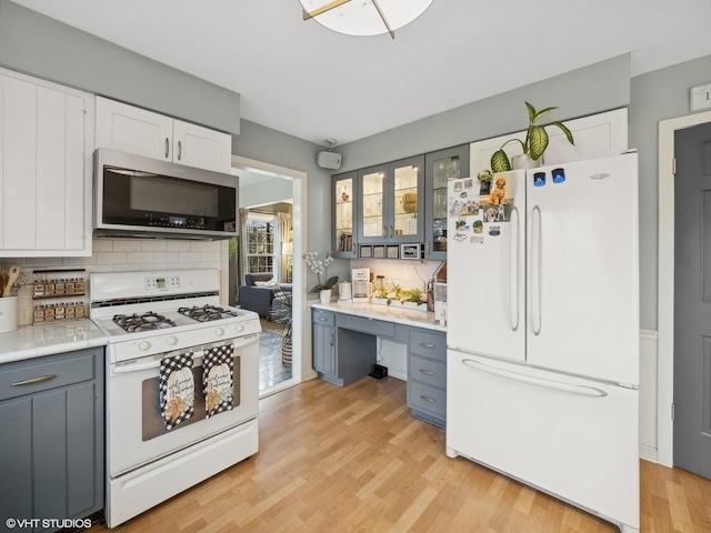 kitchen with backsplash, white appliances, gray cabinets, white cabinets, and light hardwood / wood-style floors