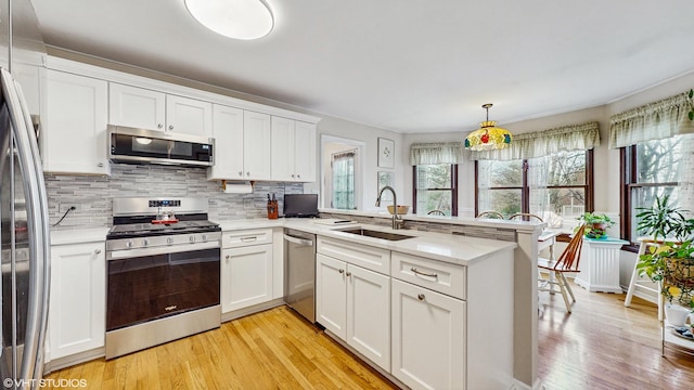 kitchen featuring kitchen peninsula, sink, light hardwood / wood-style flooring, appliances with stainless steel finishes, and white cabinetry