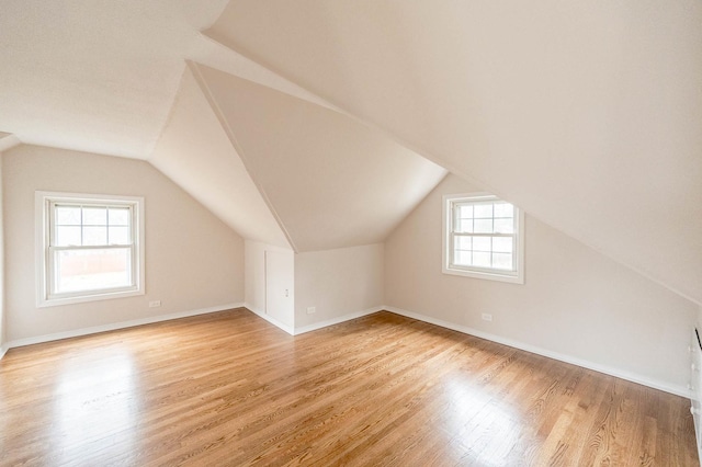 additional living space featuring light hardwood / wood-style floors, vaulted ceiling, and a healthy amount of sunlight