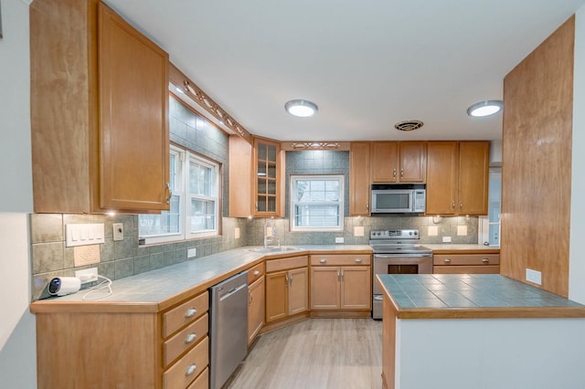 kitchen featuring tile countertops, sink, decorative backsplash, appliances with stainless steel finishes, and light hardwood / wood-style floors