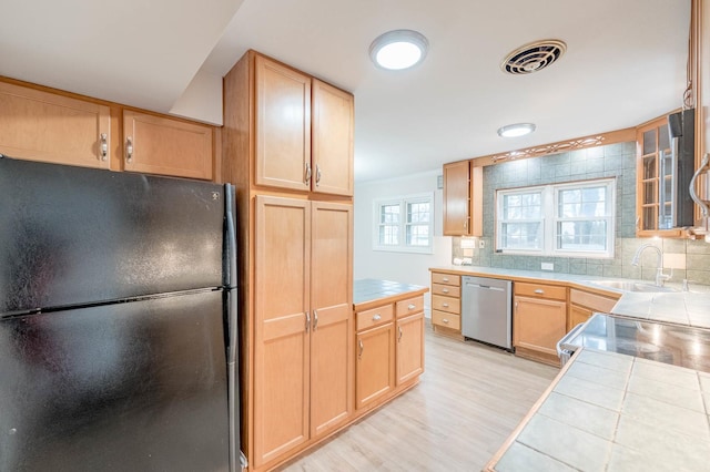 kitchen featuring tile countertops, dishwasher, black fridge, light wood-type flooring, and tasteful backsplash