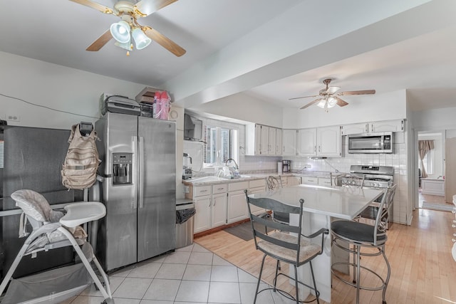 kitchen with white cabinetry, stainless steel appliances, light hardwood / wood-style flooring, a kitchen bar, and decorative backsplash