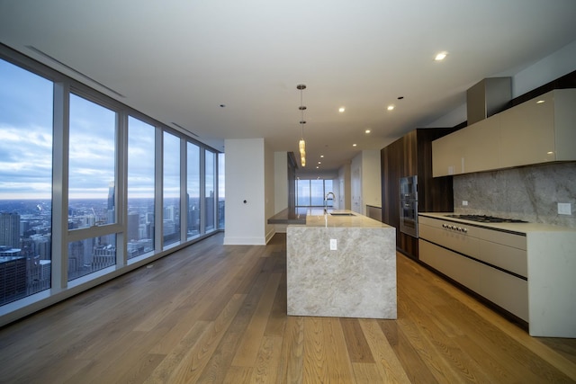 kitchen with decorative backsplash, a kitchen island with sink, sink, decorative light fixtures, and hardwood / wood-style floors