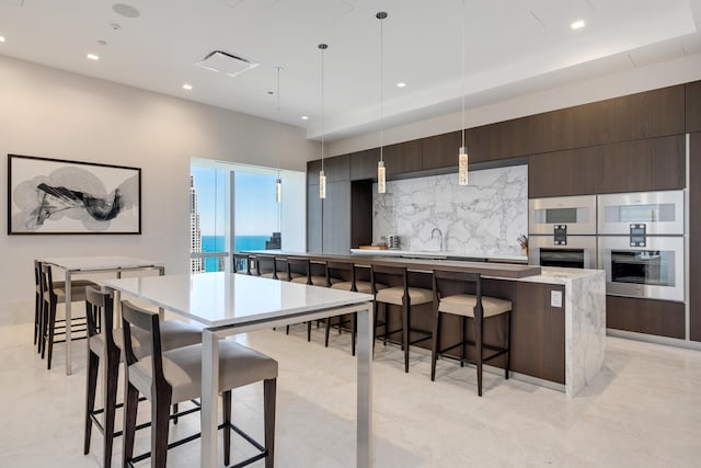 kitchen featuring a kitchen island, a kitchen breakfast bar, decorative light fixtures, dark brown cabinets, and a water view