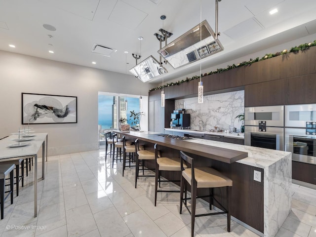 kitchen featuring decorative backsplash, pendant lighting, dark brown cabinetry, and a large island