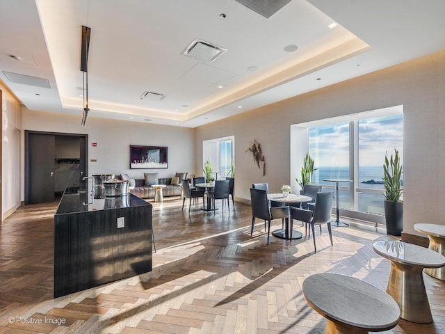 interior space with a raised ceiling, a water view, and parquet flooring