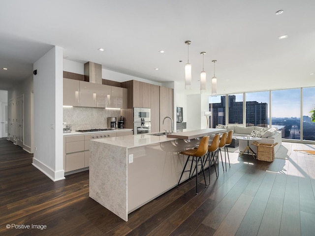 kitchen with decorative backsplash, floor to ceiling windows, wall chimney exhaust hood, pendant lighting, and an island with sink