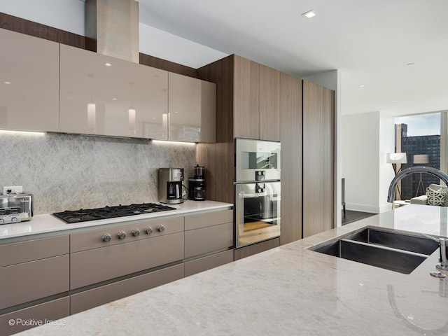 kitchen featuring backsplash, sink, multiple ovens, light stone countertops, and stainless steel gas cooktop