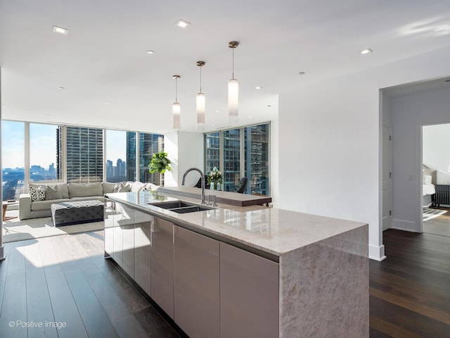 kitchen with a large island, sink, dark wood-type flooring, light stone counters, and decorative light fixtures