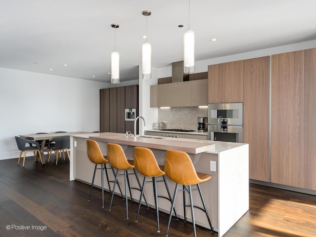 kitchen with a center island with sink, appliances with stainless steel finishes, sink, and hanging light fixtures