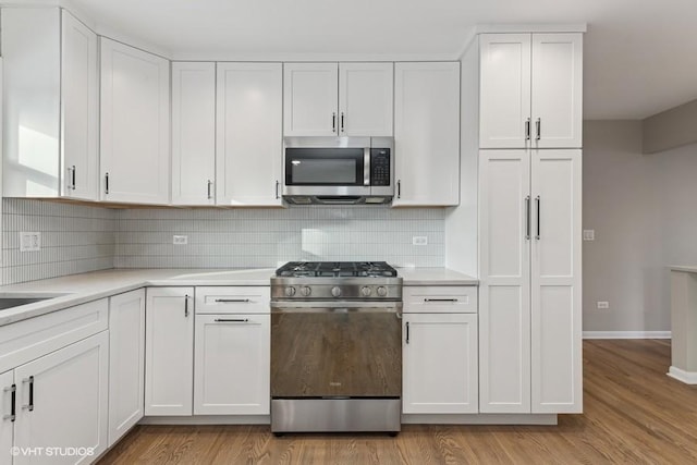 kitchen with white cabinets, light wood-type flooring, decorative backsplash, and stainless steel appliances