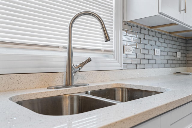 room details featuring white cabinetry, light stone countertops, sink, and decorative backsplash