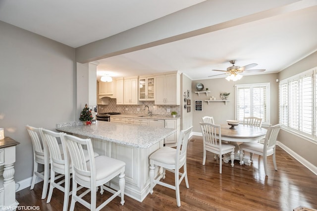 kitchen featuring ceiling fan, backsplash, kitchen peninsula, hardwood / wood-style floors, and a breakfast bar area