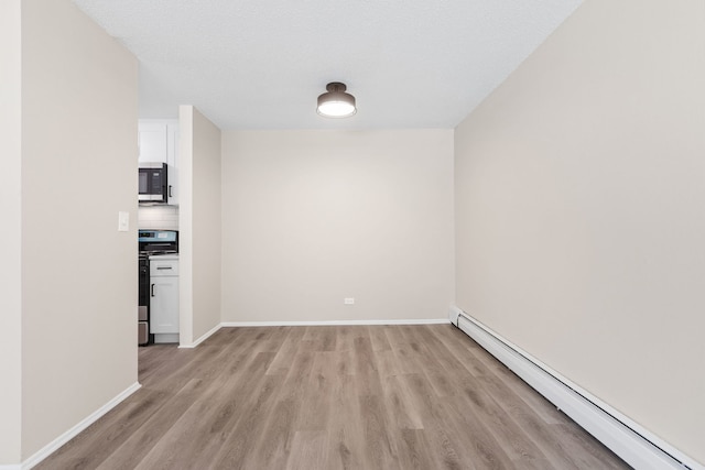 empty room with a textured ceiling, light wood-type flooring, and a baseboard radiator