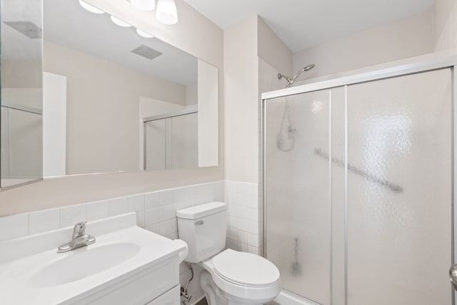 bathroom featuring vanity, a shower with door, toilet, and tile walls