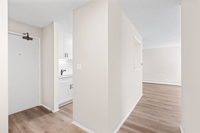 hall featuring light hardwood / wood-style flooring, a baseboard radiator, a textured ceiling, and sink