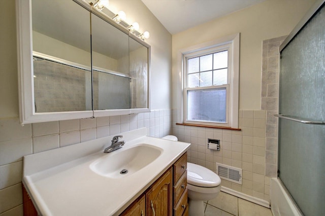 full bathroom with tile patterned flooring, enclosed tub / shower combo, toilet, vanity, and tile walls