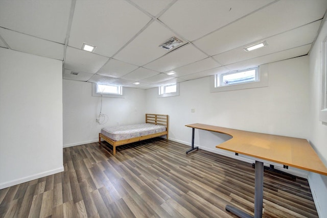 unfurnished bedroom with a drop ceiling, dark wood-type flooring, and multiple windows