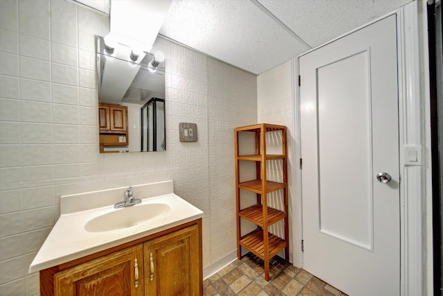 bathroom with a paneled ceiling, vanity, and tile walls