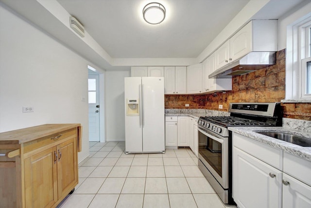 kitchen featuring white cabinetry, white refrigerator with ice dispenser, backsplash, light tile patterned floors, and stainless steel range with gas stovetop