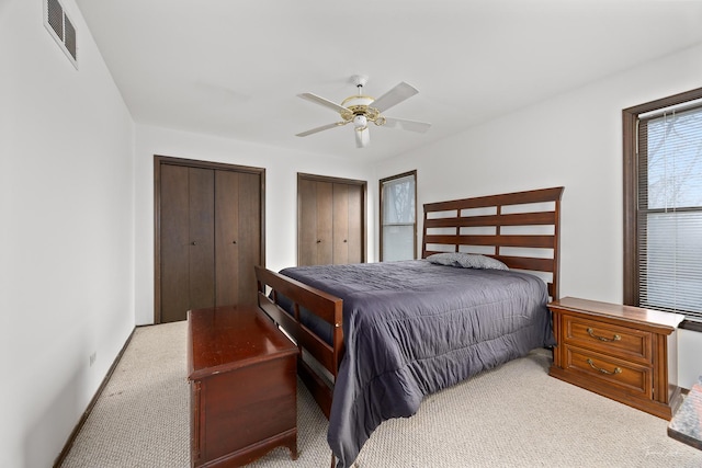 bedroom featuring light carpet, two closets, and ceiling fan