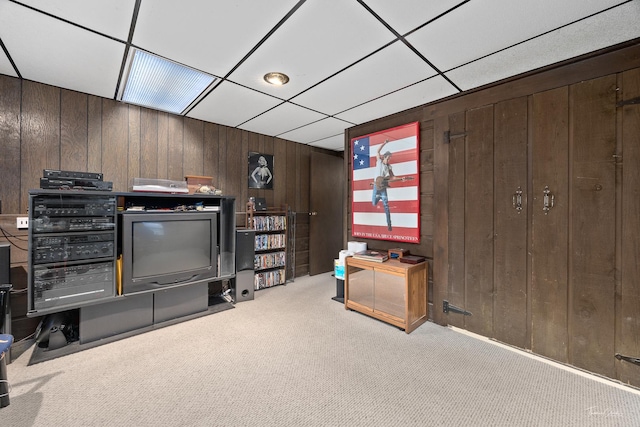 living room featuring wooden walls, a drop ceiling, and light colored carpet