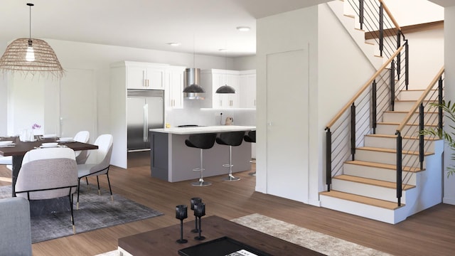 interior space with dark hardwood / wood-style flooring, wall chimney exhaust hood, decorative light fixtures, white cabinets, and built in refrigerator