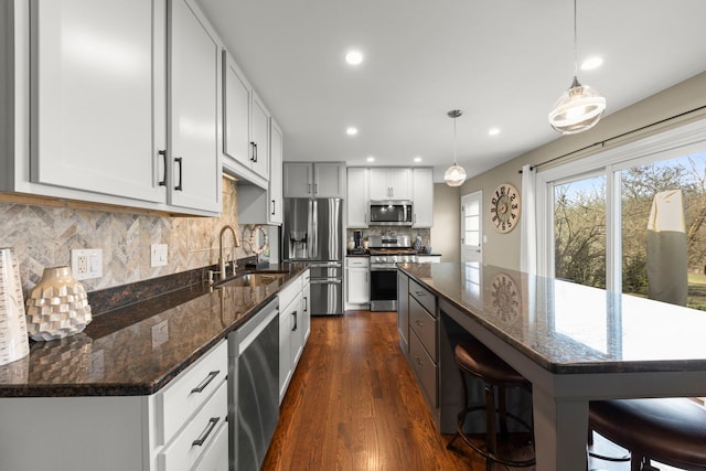 kitchen featuring stainless steel appliances, sink, white cabinetry, a kitchen island, and hanging light fixtures