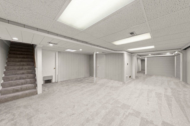 basement with wood walls, a drop ceiling, and carpet