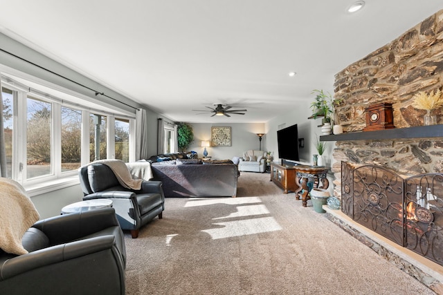 carpeted living room with a stone fireplace and ceiling fan